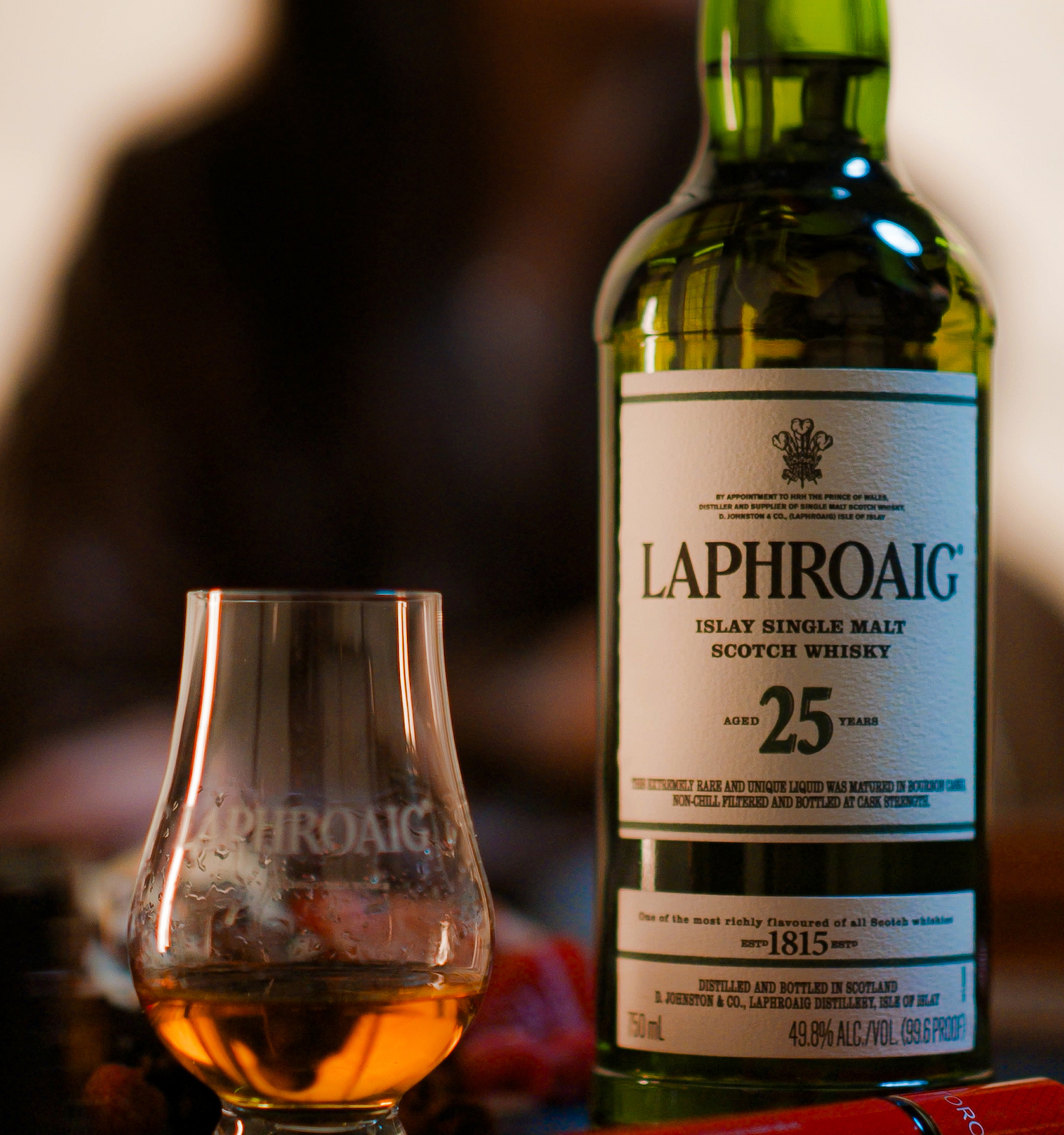 A bottle of Laphroaig 25 Year Old Scotch whisky and a glass with whisky inside, set on a table.