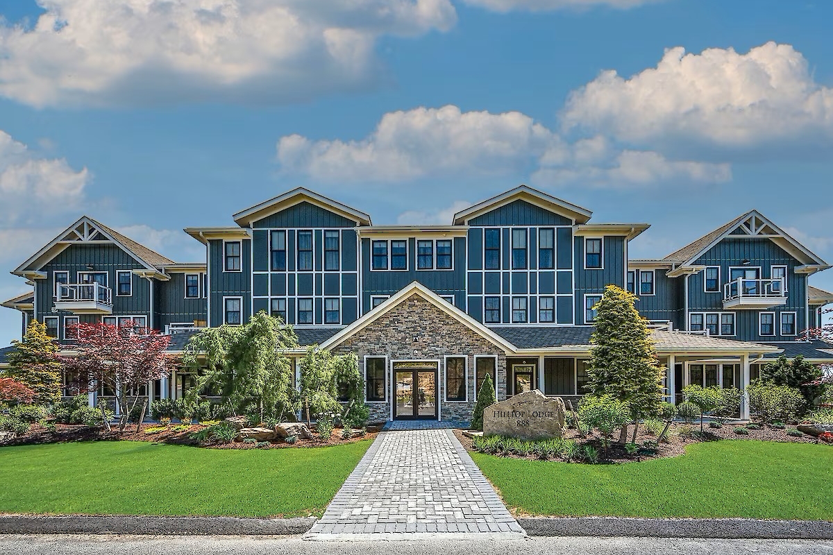 A large, modern building with a stone facade and glass windows, surrounded by landscaped gardens under a partly cloudy sky.