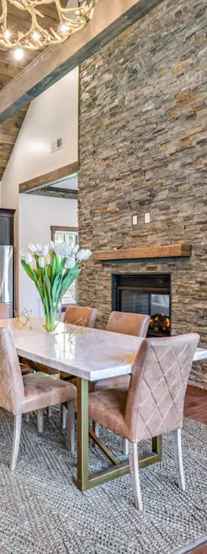 A modern open-concept living space featuring a kitchen, dining area, and living room, with stone accent walls and wood-beamed ceilings.