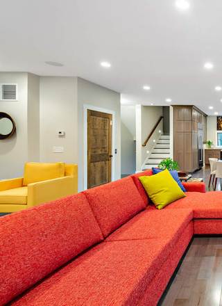 A modern living room features a red sectional sofa, yellow chair, stone fireplace, dining area, and open kitchen in the background.