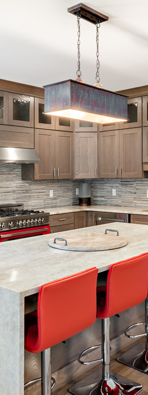 A modern kitchen with wooden cabinets, an island with red barstools, stainless steel appliances, and pendant lighting over the island.