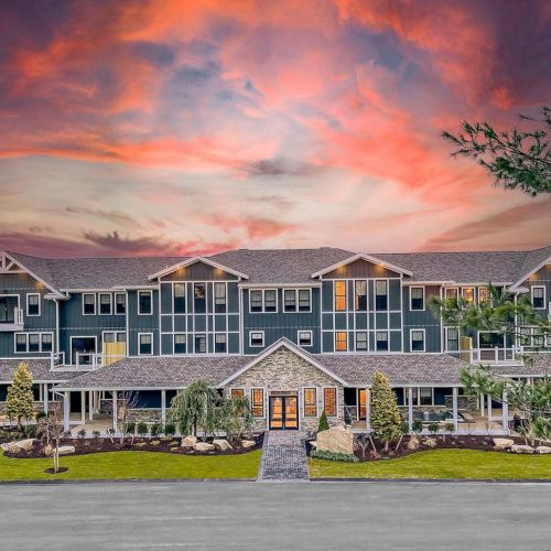 A large, modern building with multiple balconies and a well-maintained landscape, set against a dramatic, colorful sunset sky.