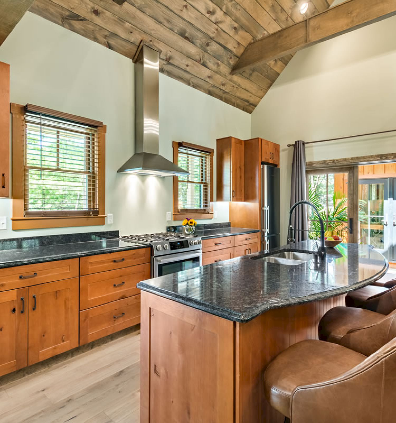 A modern kitchen with wooden cabinets, a central island with granite countertops, two bar stools, and stainless steel appliances ends the sentence.