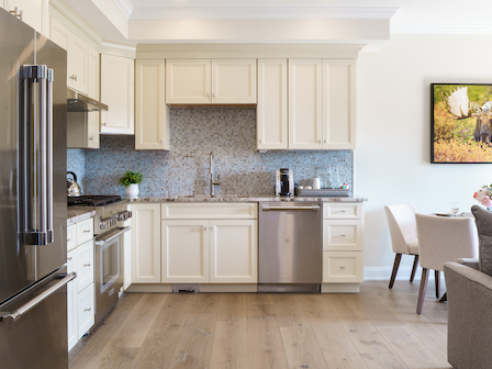 A modern kitchen with white cabinets, stainless steel appliances, and a dining area filled with natural light at The Preserve Sporting Club & Resort.