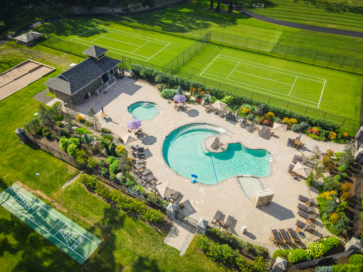 The image shows a luxurious outdoor area with a pool, tennis courts, a sports court, and a building surrounded by landscaped gardens.