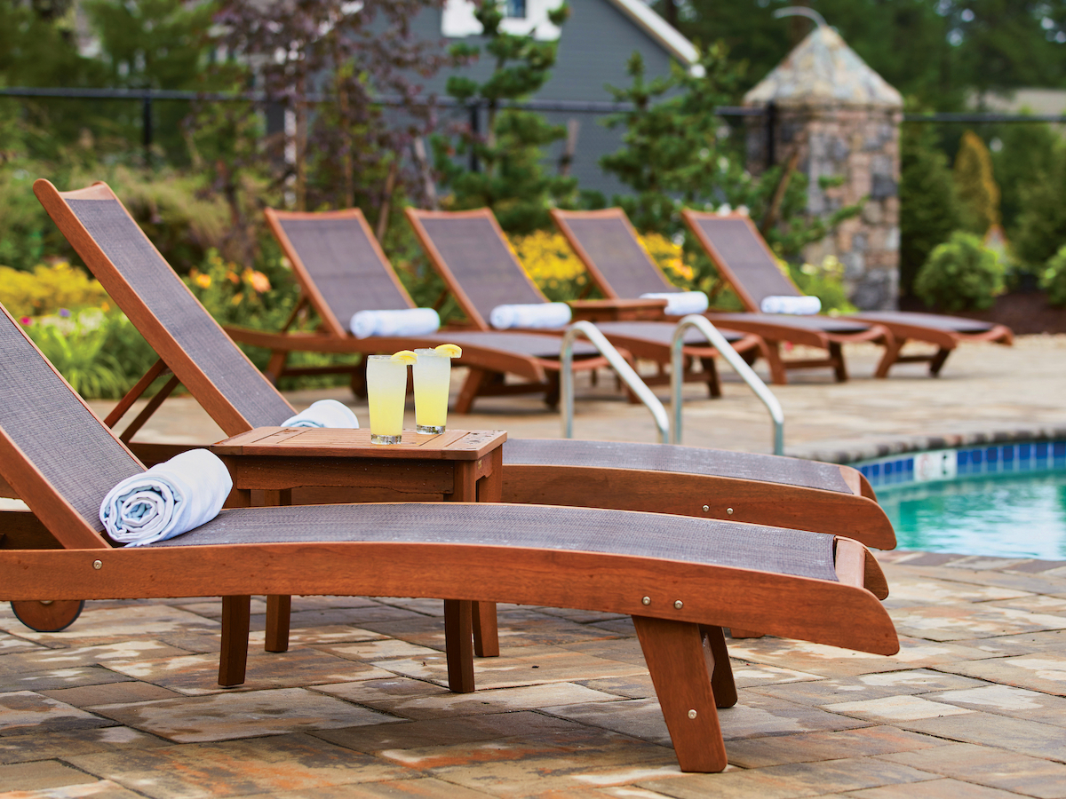 Wooden lounge chairs with towels and drinks by a poolside on a sunny day.