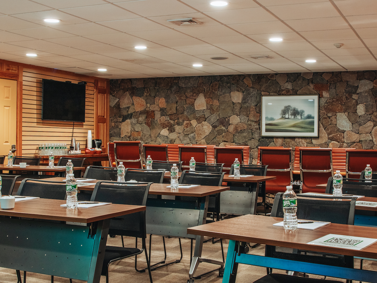 A conference room with tables and chairs, water bottles, notepads, a TV, and a stone accent wall with a framed picture.