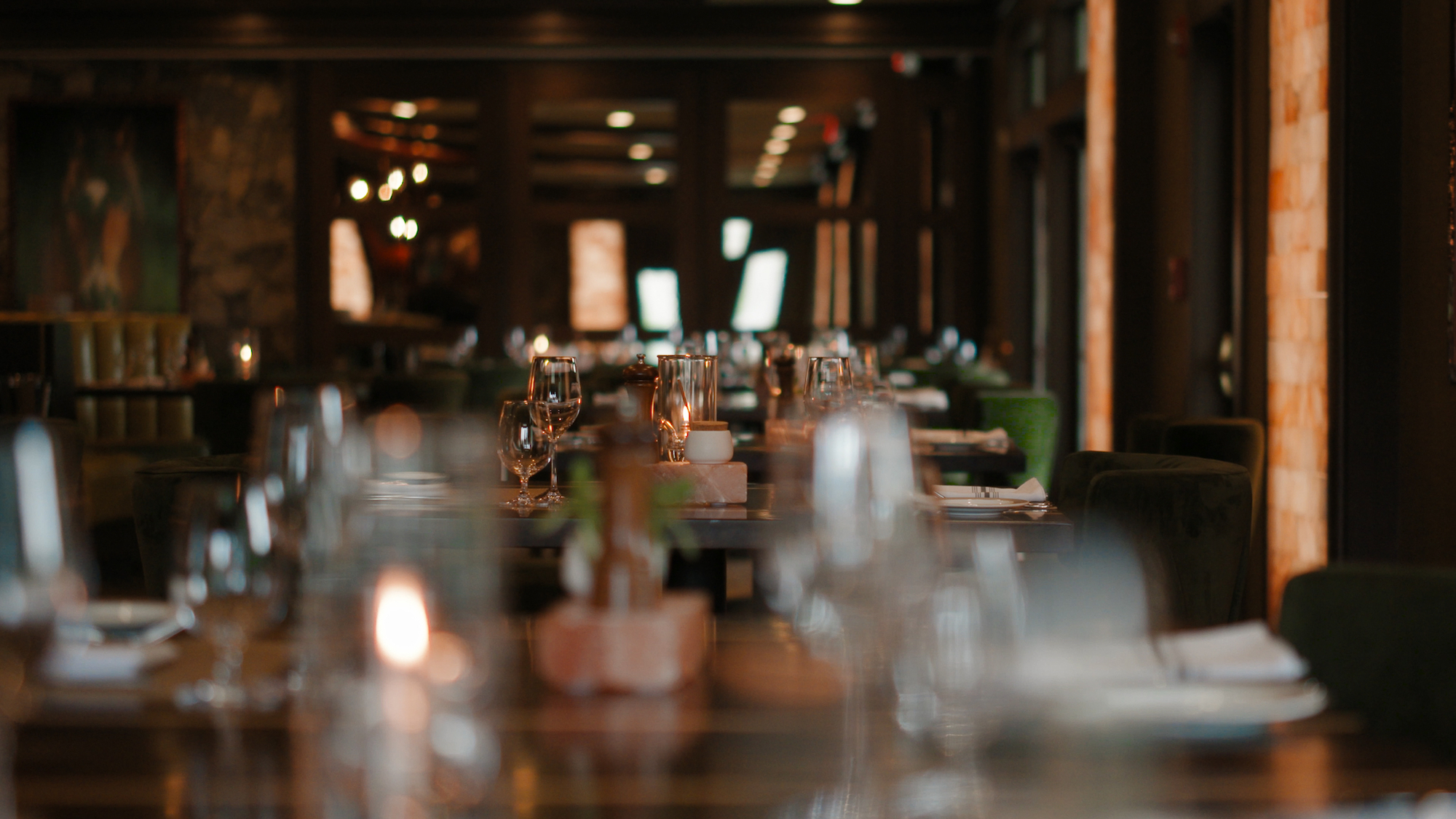 A dimly lit restaurant with neatly arranged tables, wine glasses, and cutlery, creating an inviting atmosphere for diners.