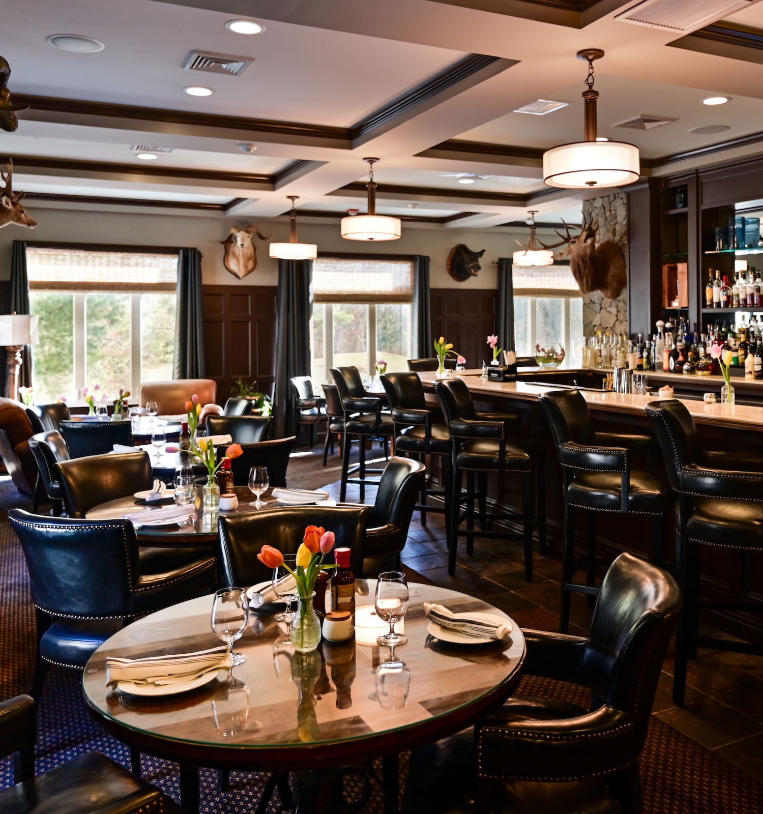 The image shows a cozy bar and restaurant with dark wood furniture, a well-stocked bar, and tables set for dining, featuring a warm, inviting ambiance.