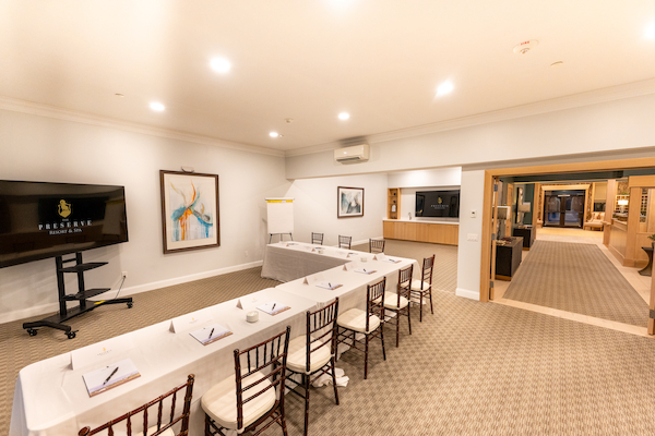 A conference room with a U-shaped table setup, chairs, a television, modern art, and notepads. An open hallway leads to other rooms.