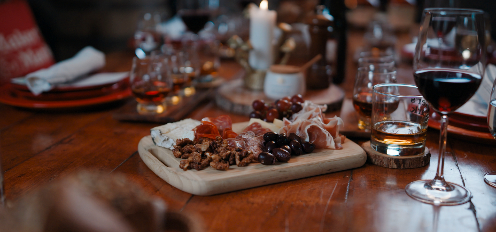 Charcuterie board with wine and whiskey glasses on a rustic wooden table.