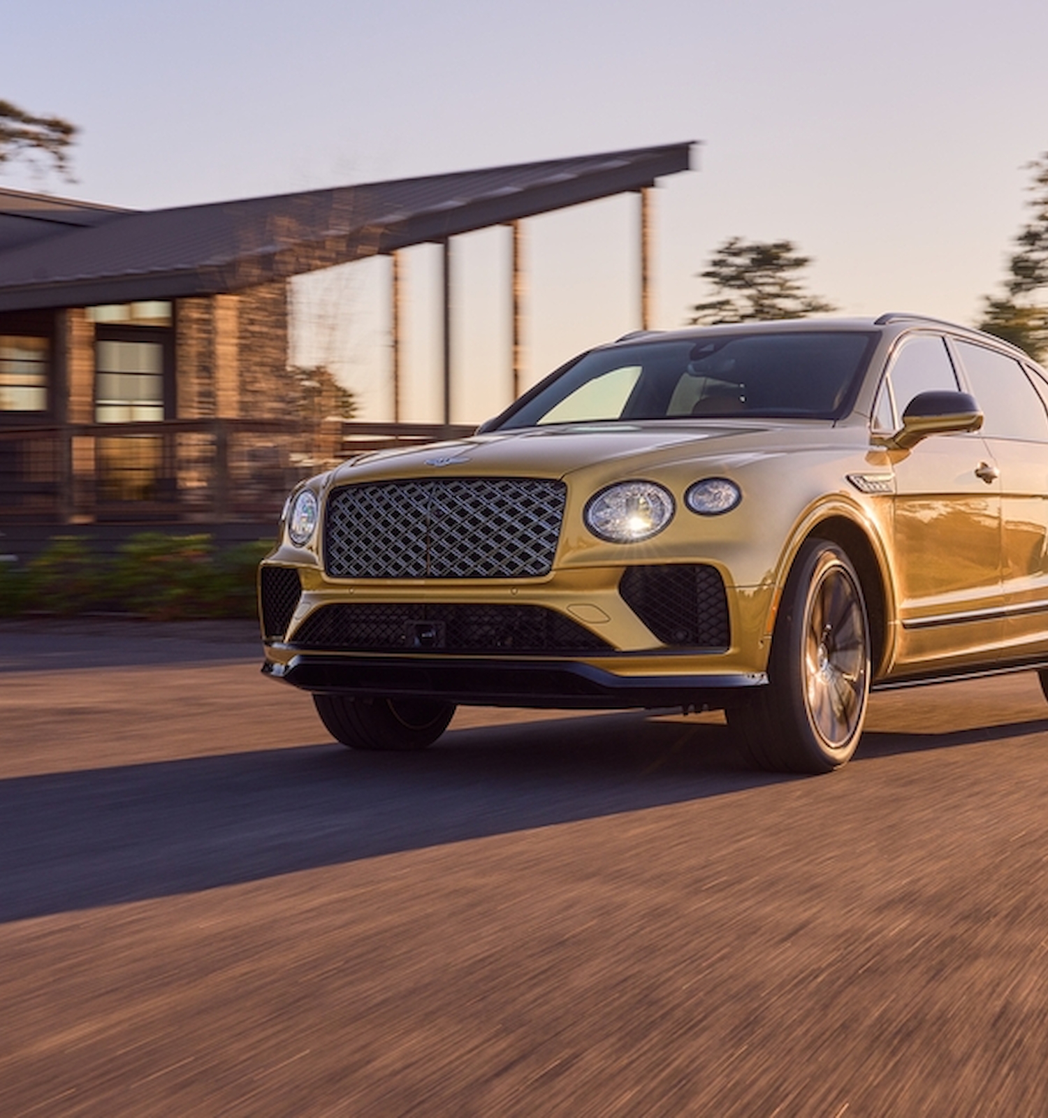 A luxury SUV is driving on a street in front of a modern house, with sunlight illuminating the scene from the side.