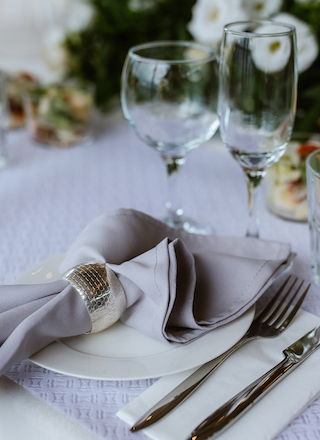 The image shows an elegant table setting with a white plate, silverware, a gray napkin in a holder, and two empty wine glasses.