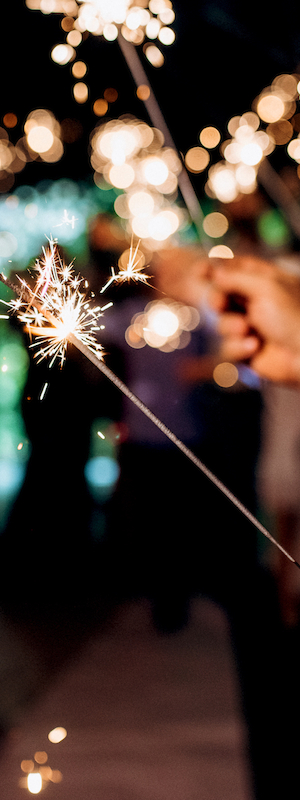 People holding sparklers in a festive or celebratory setting, creating a sparkling effect in the dark.