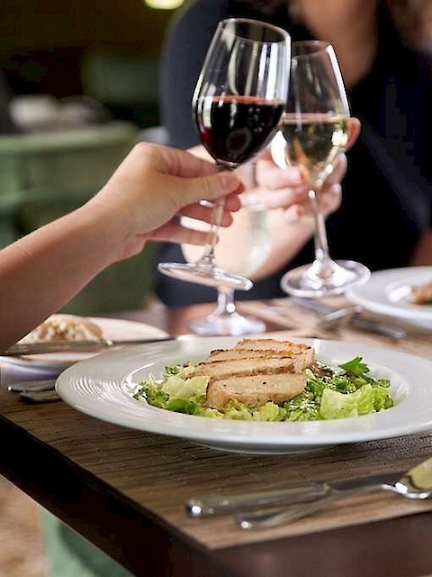 People enjoying a meal with wine, featuring plates of grilled chicken salad on a dining table.