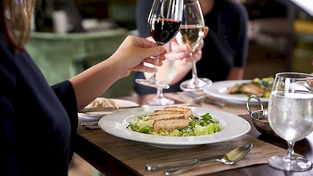 People enjoying a meal with wine, featuring plates of grilled chicken salad on a dining table.