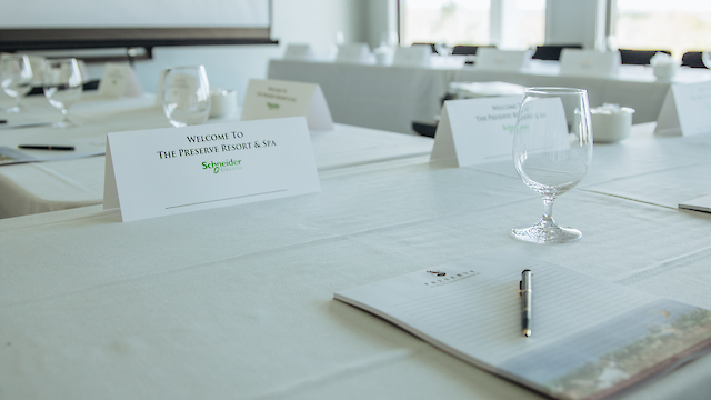 The image shows a conference room setup with notepads, pens, and glasses on a table, plus a sign reading 