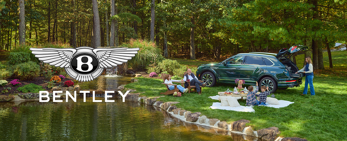 A family enjoys a picnic by a pond with a green Bentley SUV parked nearby, showcasing a serene outdoor setting.