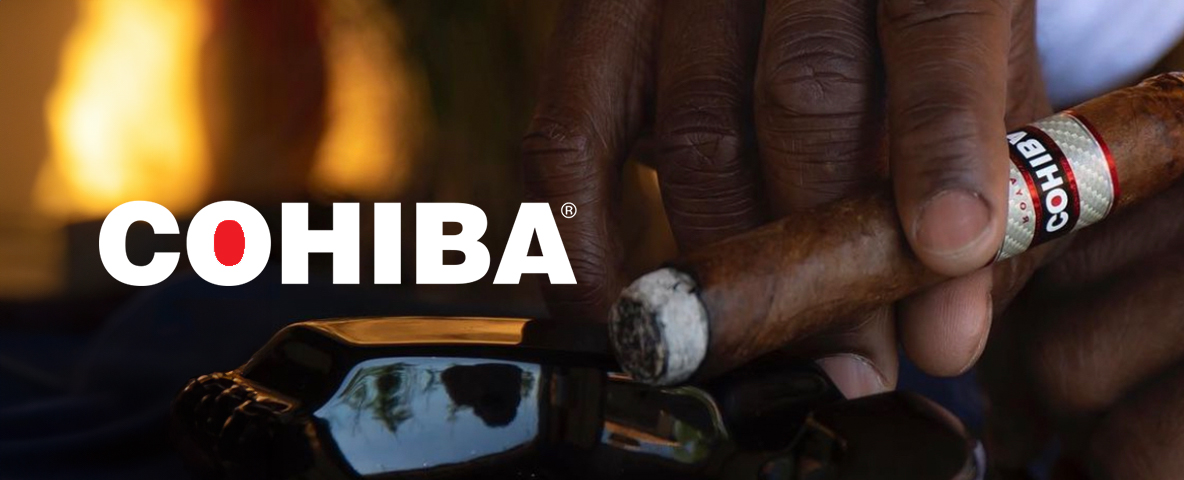 A hand holding a Cohiba cigar with the logo visible, near a black ashtray.