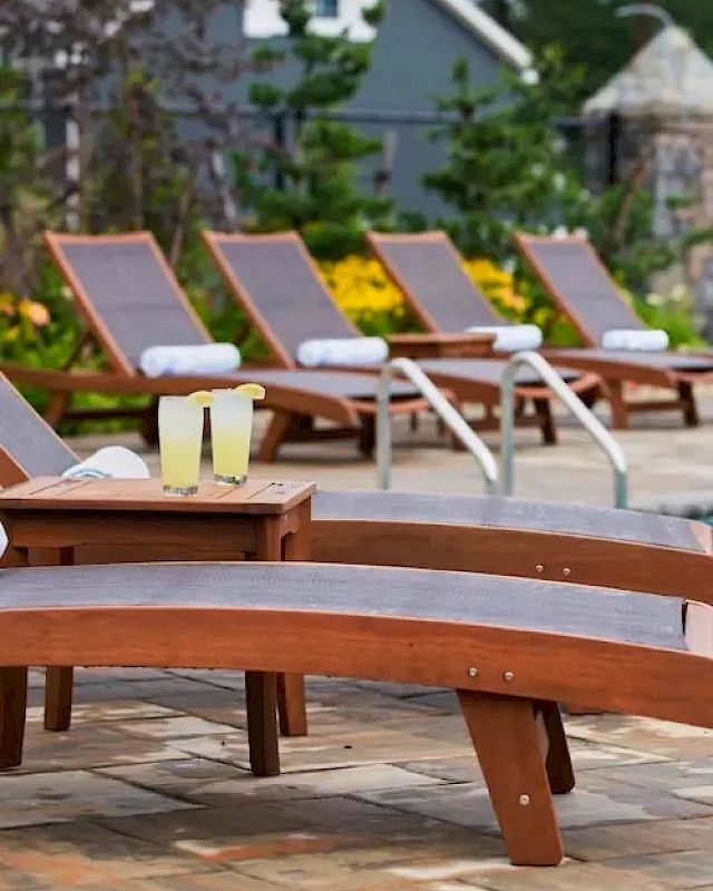 A series of lounge chairs with rolled towels are positioned around a poolside, with two glasses of lemonade on a small table in the foreground.