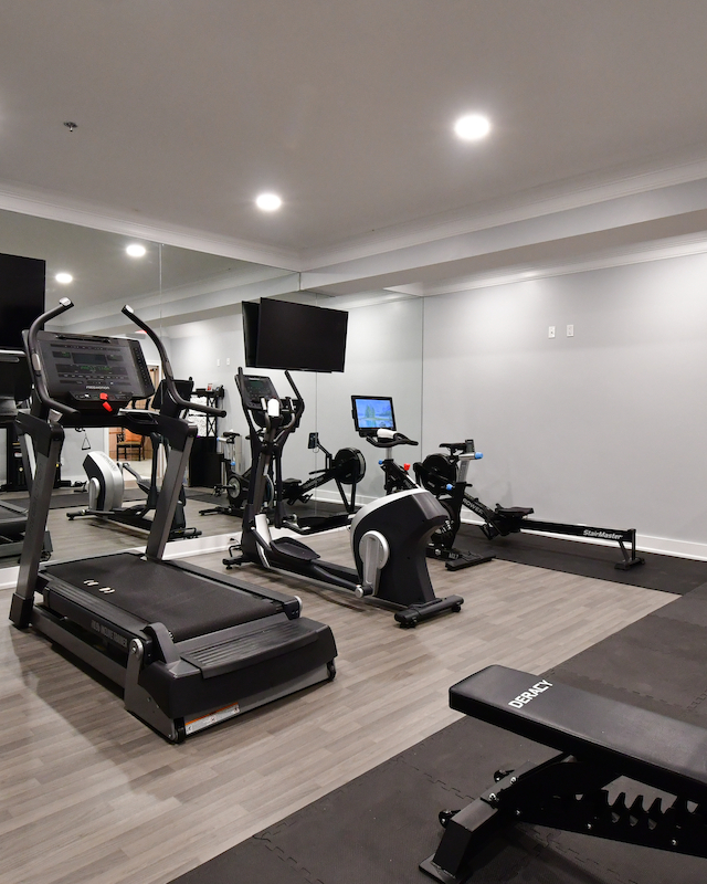 A modern gym with treadmills, stationary bikes, benches, and a towel rack. Fitness equipment is neatly arranged in the space.