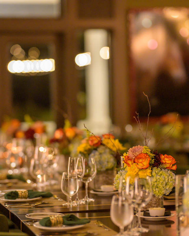 A beautifully set dining table with floral centerpieces, elegant glassware, and green chairs, evoking a warm and inviting atmosphere.