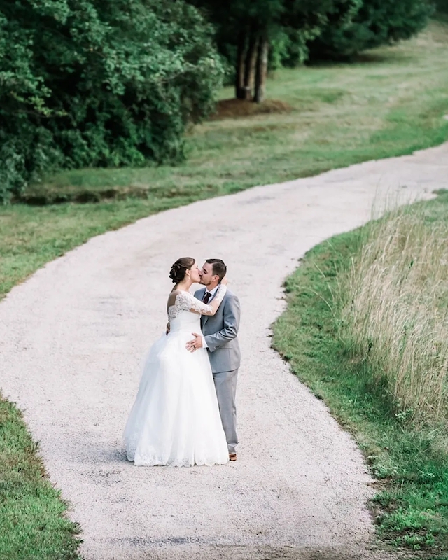 A couple in wedding attire embraces on a winding path surrounded by greenery, creating a romantic and scenic atmosphere.