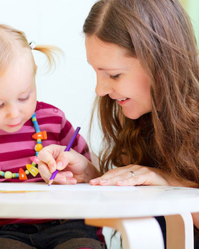 A child and an adult are coloring together at a table with colored pencils, creating a joyful and creative atmosphere.