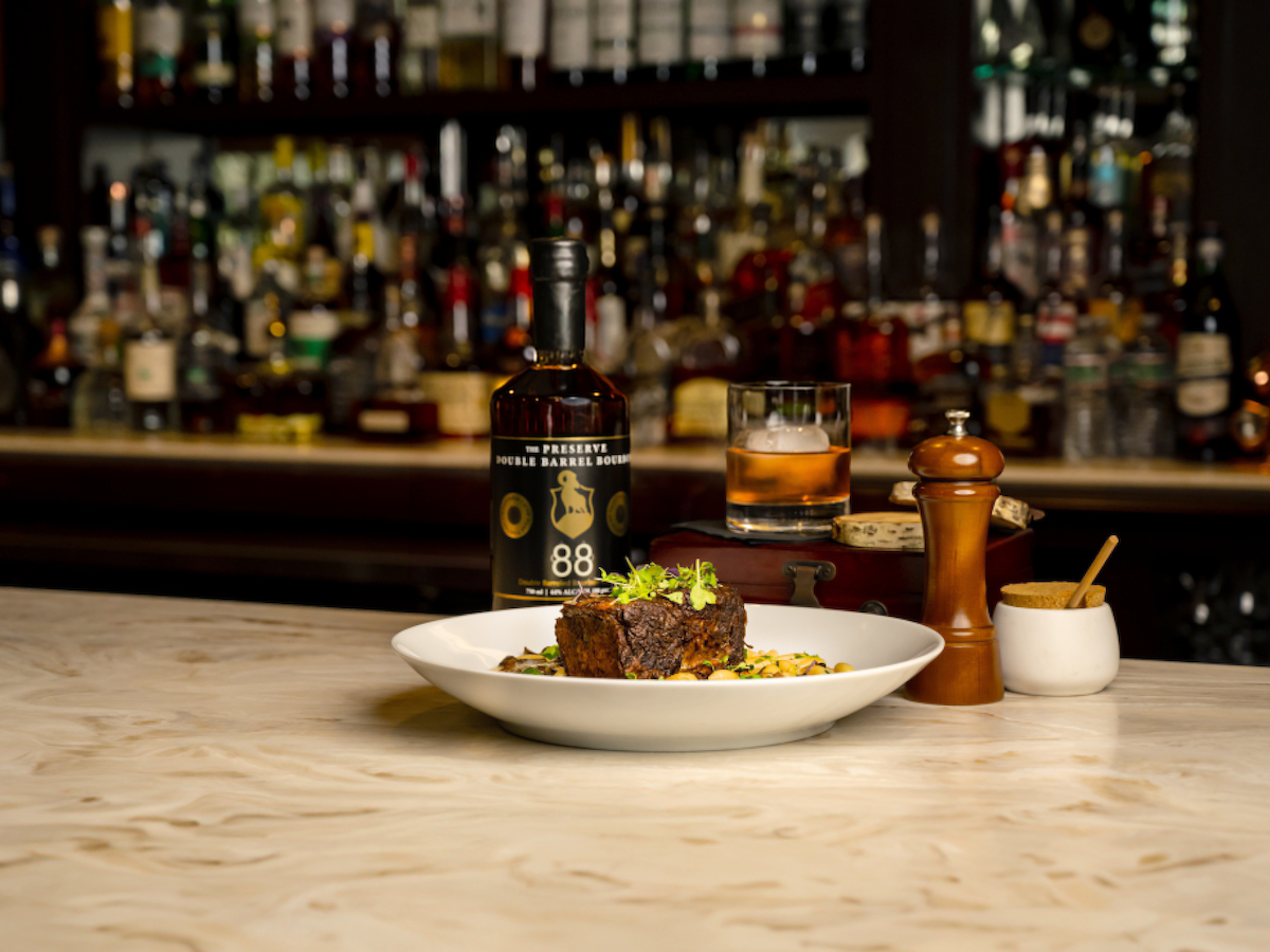 A dish and whiskey bottle on a bar counter, with seasoning and a background of various liquor bottles on shelves.