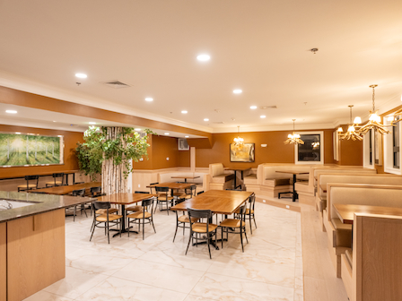 The image shows a modern restaurant interior with wooden tables, chairs, booths, and warm lighting, creating a cozy dining atmosphere.