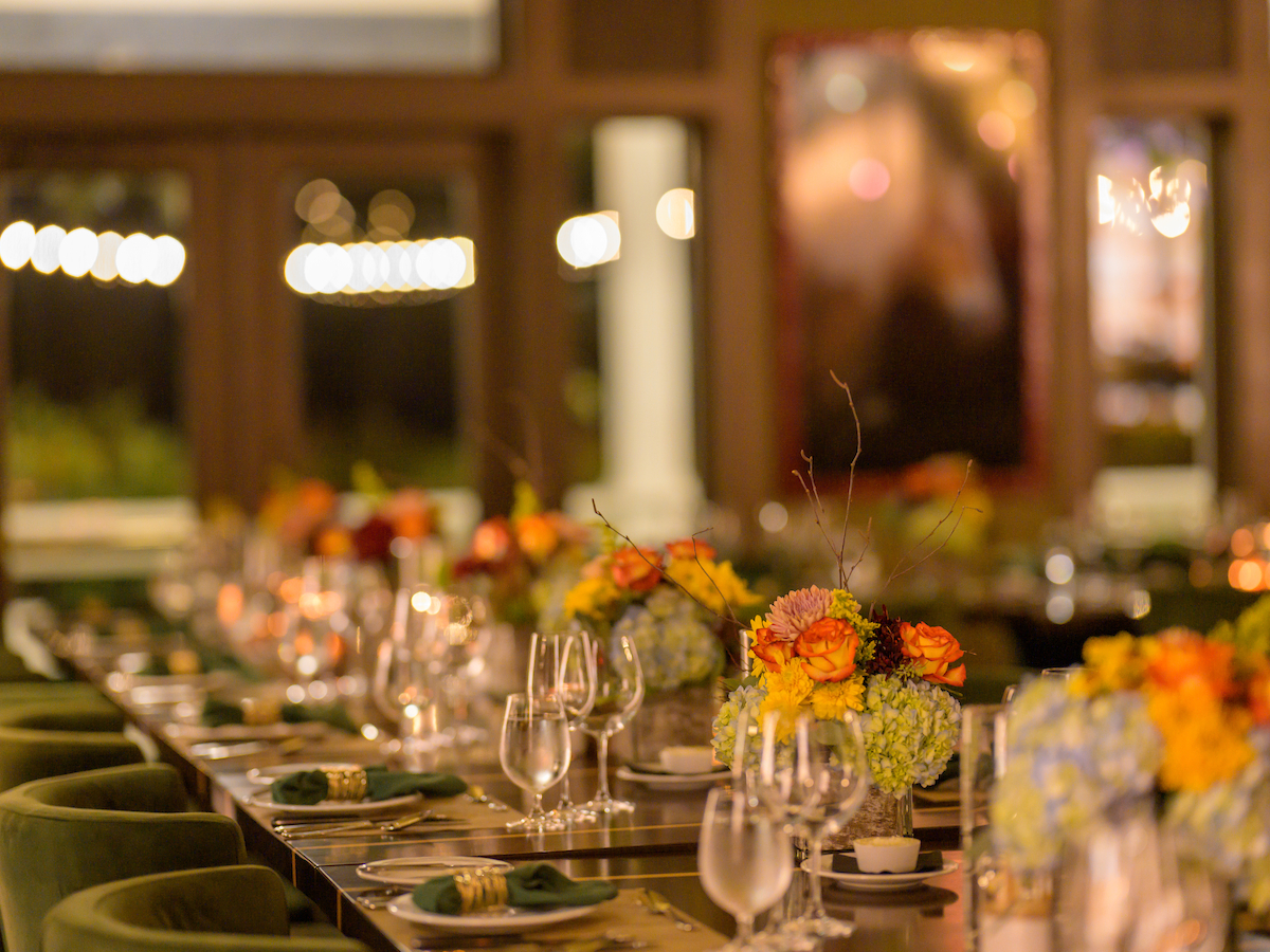 A beautifully set dining table with elegant glassware, vibrant floral centerpieces, and a warm, inviting atmosphere in a softly lit room.